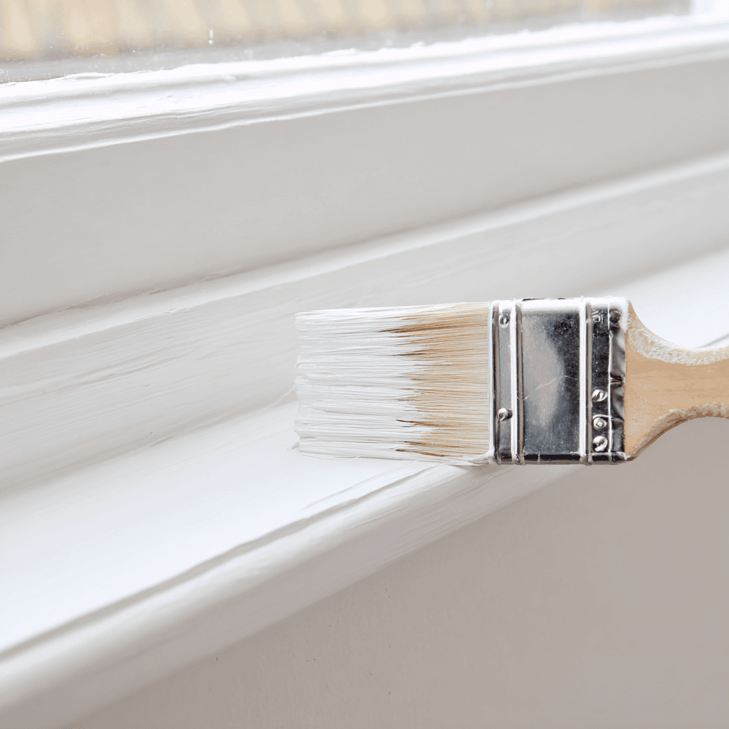 Paintbrush applying fresh white paint to window trim before property sale Paintbrush applying fresh white paint to window trim before property sale